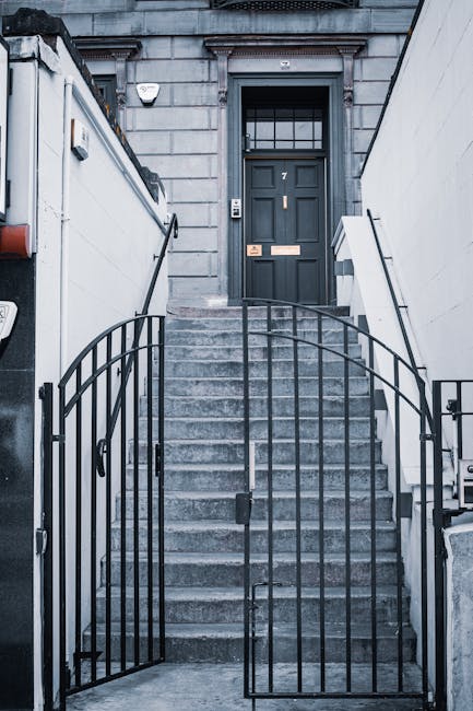 A steep residential street in Maida Hill with narrow stairs leading up between white and brick buildings, some with balconies and greenery, under a clear blue sky. A streetlamp is situated along the sidewalk, which is adjacent to the steps. The photograph captures the outdoor environment during daytime, highlighting the challenging access for furniture transport and home relocation activities. The buildings are multi-story with a variety of window styles, and vegetation is visible on some structures. This setting illustrates common issues faced during removals for properties with limited stairwell space, where careful planning of furniture handling and logistics is essential, as often managed by [COMPANY_NAME], Man With a Van Maida Hill, for efficient packing and moving procedures.
